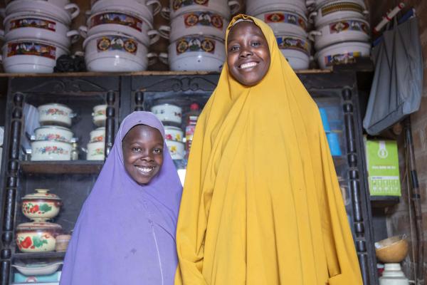 Two Nigerian women, inside their store, are smiling at the camera.